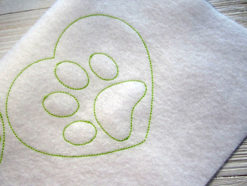 May include: A white fabric heart with a green embroidered paw print inside.