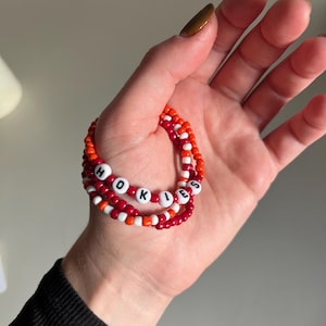May include: Three red and orange beaded bracelets with the word "HOKIES" spelled out in white beads.