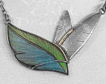 May include: A silver necklace featuring a leaf design. The necklace has a chain and pendant with three leaf shapes. The largest leaf is blue and green, while the other two are silver with etched details. A gold accent is present.