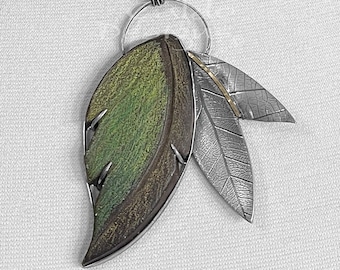 May include: A silver necklace featuring a pendant with three leaf designs. The largest leaf is green and brown, while the other two are silver. The necklace has a silver chain.