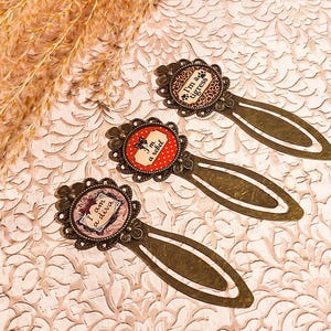 May include: Three gold-toned metal bookmarks with colorful, patterned designs. The bookmarks feature the text "I'm a tigress", "I'm a diva", and "I'm a rebel".