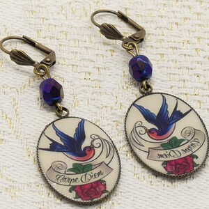 May include: A pair of dangle earrings with a blue glass bead and a round charm featuring a swallow tattoo with the text "Carpe Diem" and a red rose.
