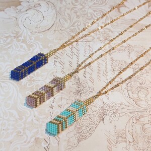 May include: Three gold chain necklaces with different colored beaded pendants. The pendants are geometric patterns in blue, pink, and turquoise.