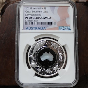 Peut inclure: Une pièce de monnaie australienne de 1 $ de 2021, Great Southern Land, classée PF 70 Ultra Cameo par NGC. La pièce présente un motif argenté d'une carte de l'Australie entourée de diverses créatures marines.