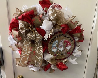 May include: A Christmas wreath with red, white, and brown burlap ribbon, a white mesh base, and a round sign that says "Happy Holidays" with three gnomes on it.