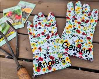 May include: A pair of white gardening gloves with a floral print in red, yellow, and black. The gloves are personalized with the text "Angie's" and "Garden".