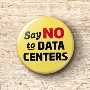 May include: A yellow button with the text "Say NO to DATA CENTERS" in black and red. The button is round and sits on a light brown, textured surface.