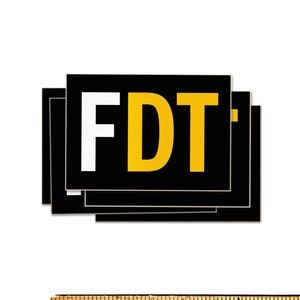 Może przedstawiać: Stos czarnych kwadratowych naklejek z literami "FDT" w kolorze białym i złotym. Naklejki są ułożone na białym tle z drewnianą linijką u dołu, mierzącą do 10 cm.