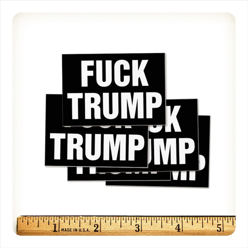 May include: A collection of black rectangular stickers with the words "FUCK TRUMP" in bold white capital letters. A wooden ruler is at the bottom of the image.