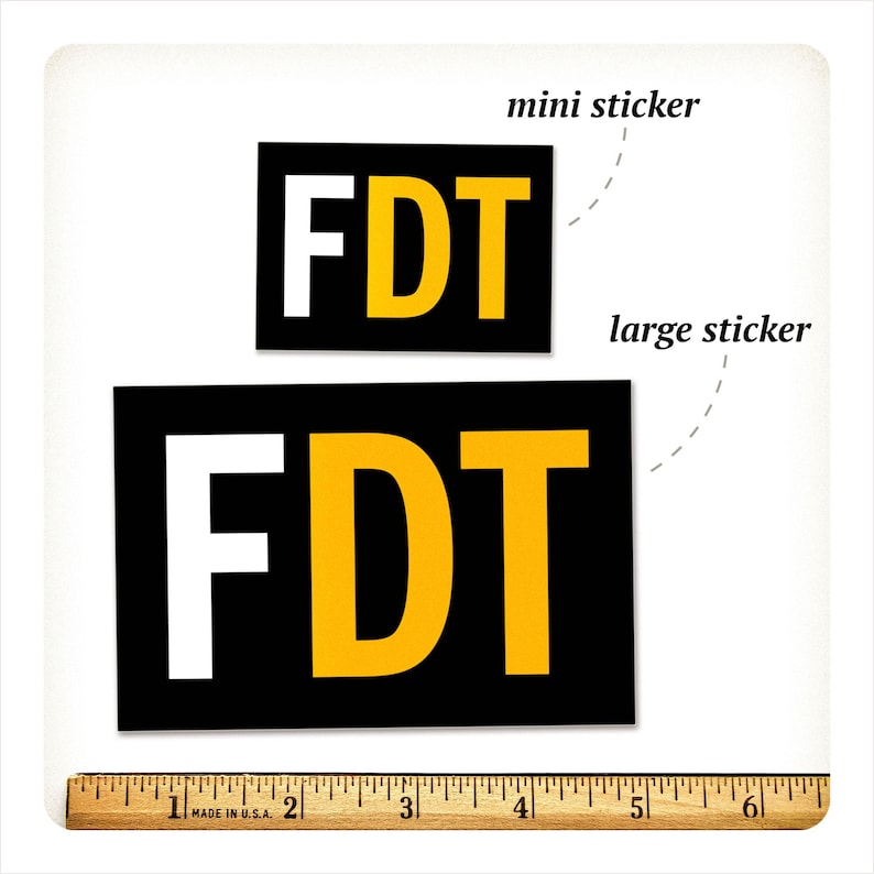 Może przedstawiać: Dwie czarne prostokątne naklejki z literami "FDT" w kolorze białym i ż&oacute;łtym. Mniejsza naklejka jest oznaczona jako "mini sticker", a większa jako "large sticker". Na dole znajduje się linijka w calach, około 15 cm.