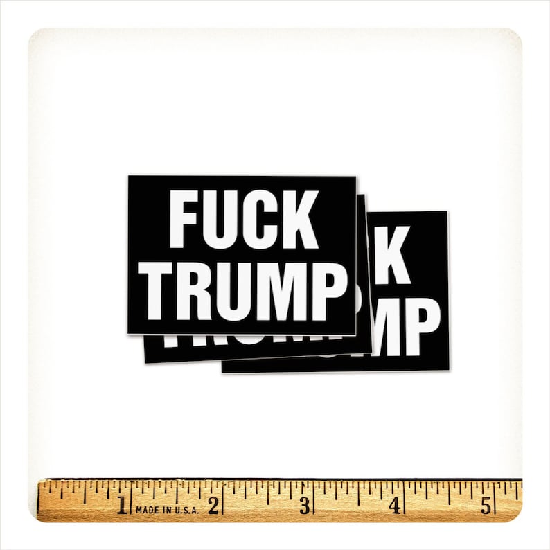 May include: A stack of black rectangular stickers with the words "FUCK TRUMP" in bold white capital letters. A wooden ruler with inch measurements is at the bottom of the image.