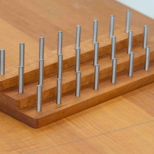 May include: A wooden stand with three tiers holds a collection of silver metal rods. The stand is made of light brown wood and has a natural finish.