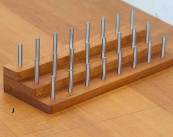 May include: A wooden stand with three tiers holds a collection of silver metal rods. The stand is made of light brown wood and has a natural finish.