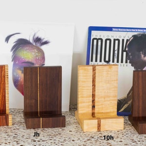 May include: Four wooden record stands with a single vertical groove down the center. The stands are made of different types of wood, including walnut, maple, and cherry. The stands are labeled Kh, Jh, 10h, and 6h.