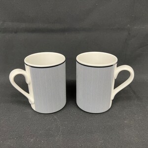 May include: Two white ceramic mugs with black vertical stripes. The mugs have a simple design and are perfect for everyday use.