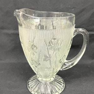 May include: A clear glass pitcher with a textured floral design and a fluted base.