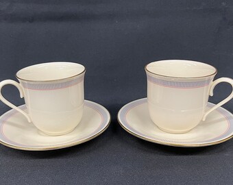 May include: Two white porcelain teacups and saucers with a blue and red stripe design and gold trim.