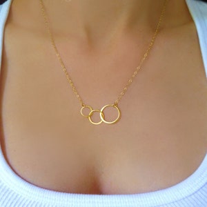 May include: A gold necklace with three interlocking circles. The circles are different sizes and are connected to a delicate gold chain.