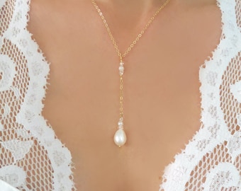 May include: A delicate gold chain necklace with a single pearl pendant and small pearl accents. The necklace is worn by a model with a white lace top.