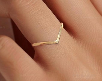 May include: A gold-colored V-shaped ring on a finger.