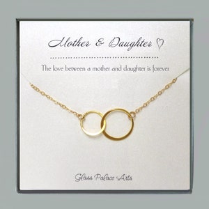May include: Gold necklace with two interlocking circles, presented in a white box with the text "Mother & Daughter" and "The love between a mother and daughter is forever". The box also includes the text "Glass Palace Arts".