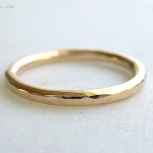 May include: A simple gold band ring with a hammered texture.
