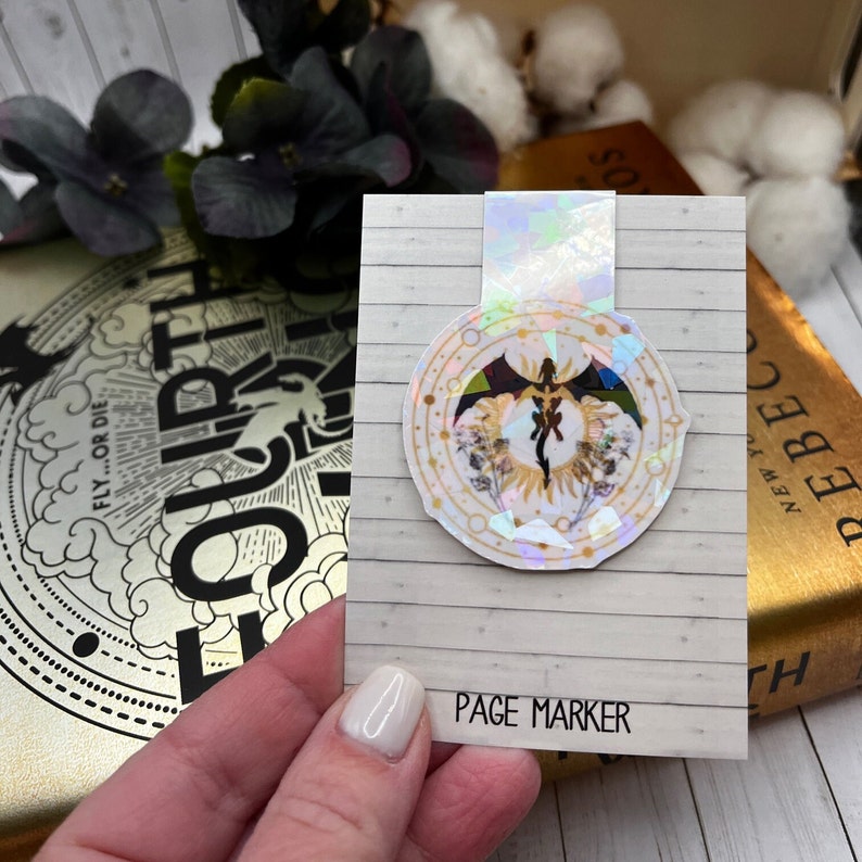 May include: A white page marker with a holographic dragon design. The dragon is black and gold with a white background. The design is surrounded by a circle of gold and white flowers. The text "PAGE MARKER" is printed on the bottom of the marker.