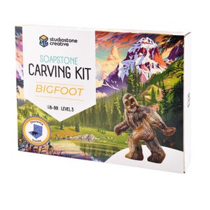 Peut inclure: Un kit de sculpture en stéatite pour Bigfoot, avec un diorama à l'intérieur. La boîte présente une illustration colorée d'un paysage de montagne et une figurine Bigfoot sculptée. Le kit est pour les âges 8-99 et est de niveau 3.