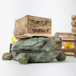 Soapstone turtle carrying wood box that says "turtle service"