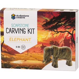 May include: Soapstone carving kit featuring an elephant. The box has a colorful illustration of an African savanna sunset with a tree silhouette. The kit includes a soapstone elephant carving and tools for carving.
