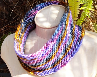 May include: A colorful knitted neck warmer in shades of purple, blue, pink, and gold. The neck warmer is made of a soft, textured yarn and is perfect for keeping warm in the winter.