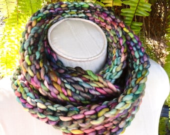 May include: A colorful knitted infinity scarf with a variety of shades of green, blue, purple, pink, and yellow. The scarf is made with a chunky yarn and has a thick, textured look.