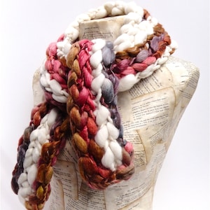 May include: A chunky knit scarf in white, brown, pink, and grey. The scarf is made of soft yarn and has a unique braided design.