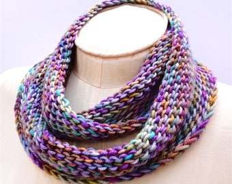 May include: A colorful knitted infinity scarf in shades of purple, teal, brown, and cream. The scarf is made with a chunky yarn and has a textured stitch pattern.