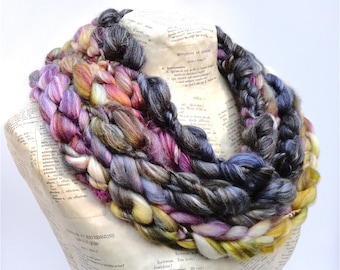 May include: A multi-colored yarn necklace with shades of purple, blue, gray, yellow, and white. The yarn is braided and twisted into a thick, chunky rope.