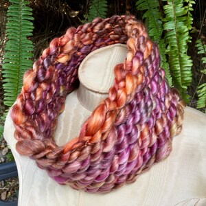 May include: A thick, chunky knit cowl in shades of orange, pink, and brown. The cowl is made of a soft, fuzzy yarn and is perfect for keeping warm in the winter.