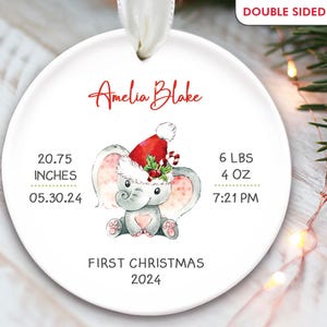 Pu&ograve; includere: Un ornamento natalizio rotondo bianco con un elefante grigio che indossa un cappello rosso di Babbo Natale. L'ornamento &egrave; personalizzato con il nome "Amelia Blake", la data "05.30.24", l'ora "7:21 PM" e il testo "Primo Natale 2024".