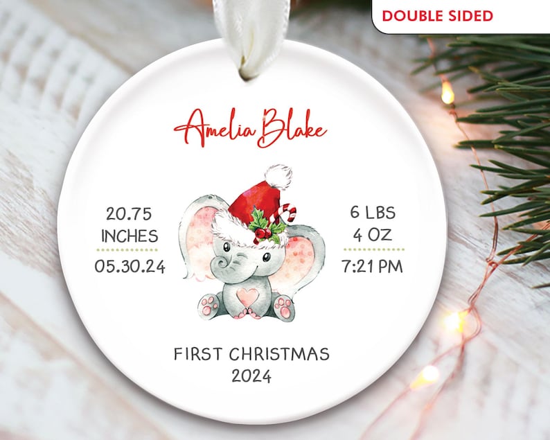 Pu&ograve; includere: Un ornamento natalizio rotondo bianco con un elefante grigio che indossa un cappello rosso di Babbo Natale. L'ornamento &egrave; personalizzato con il nome "Amelia Blake", la data "05.30.24", l'ora "7:21 PM" e il testo "Primo Natale 2024".