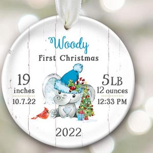Pu&ograve; includere: Un ornamento natalizio rotondo bianco con uno sfondo in legno. Presenta un elefante dei cartoni animati che indossa un cappello di Babbo Natale blu e tiene un bastone di zucchero. L'ornamento &egrave; personalizzato con il nome "Woody", il testo "Primo Natale", e le statistiche di nascita del bambino: 19 pollici, 5 LB 12 once, 10.7.22, 12:33 PM, e 2022.