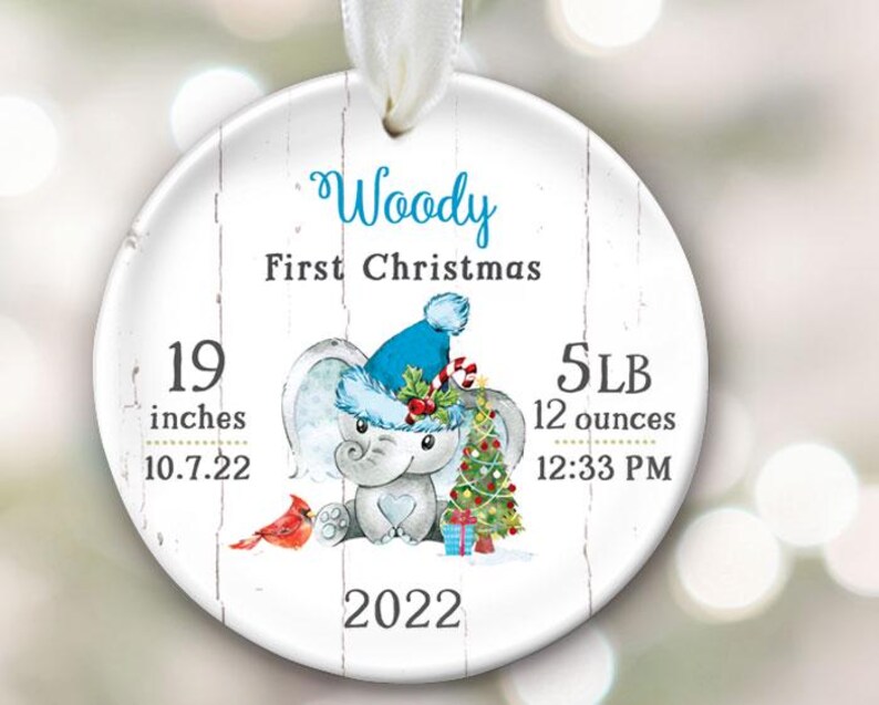 Pu&ograve; includere: Un ornamento natalizio rotondo bianco con uno sfondo in legno. Presenta un elefante dei cartoni animati che indossa un cappello di Babbo Natale blu e tiene un bastone di zucchero. L'ornamento &egrave; personalizzato con il nome "Woody", il testo "Primo Natale", e le statistiche di nascita del bambino: 19 pollici, 5 LB 12 once, 10.7.22, 12:33 PM, e 2022.
