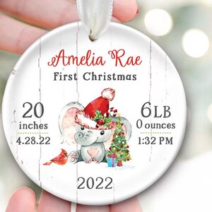 Pu&ograve; includere: Addobbo natalizio bianco con un adorabile elefante che indossa un cappello di Babbo Natale e tiene un albero di Natale. L'addobbo dice "Amelia Rae First Christmas" e include le statistiche di nascita del bambino: 20 pollici, 6 lb 0 oz, 4.28.22, 1:32 PM e 2022.