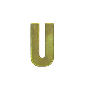 Op de afbeelding: Een verweerde, gouden metalen letter "U". De hoofdletter heeft een verweerde afwerking, met zichtbare slijtage, wat wijst op een verouderde of vintage uitstraling. De achtergrond is effen wit.