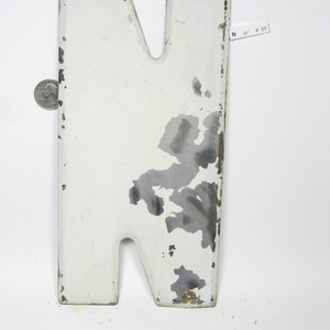 Op de afbeelding: Witte metalen letter N met wat roest en afbladderende verf. De letter is ongeveer 25 cm hoog.