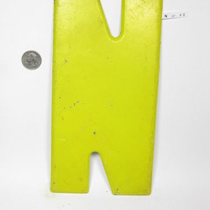 Op de afbeelding: Een grote, felgele metalen letter N. De letter is licht verweerd en heeft een paar kleine krassen. De letter is 25,4 cm hoog en 5,1 cm breed.