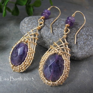 May include: A pair of gold wire wrapped earrings with amethyst gemstones. The earrings feature a delicate wire design and dangle from gold hooks.