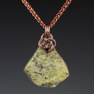 Puede incluir: Un collar de cadena de cobre con un colgante de piedra verde y blanca. El colgante está sujeto por un nudo de alambre de cobre.