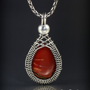 May include: A silver chain necklace with a teardrop-shaped pendant featuring a red jasper stone wrapped in silver wire. The pendant has a silver bead at the top.