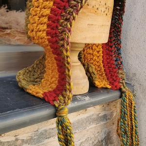 May include: A colourful crocheted hat with a long, pointed top and tassels. The hat is made in a variety of colours, including red, orange, yellow, green, and purple.