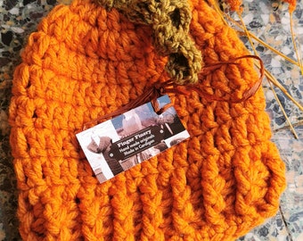 Könnte beinhalten: Orangefarbener, gehäkelter Kürbis-Hut mit einem grünen, gehäkelten Stiel und Blättern. Der Hut ist handgefertigt und hat ein Etikett mit der Aufschrift "Finger Finery Hand made originals Made in Cardigan".