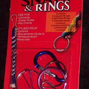 May include: A Rexlace Snaps & Rings craft kit on a red backing card. The package contains three lanyard snaps, two split key rings, and one climber's hook. The text on the card lists uses for lanyards, zipper grabs, and key chains in English and French.